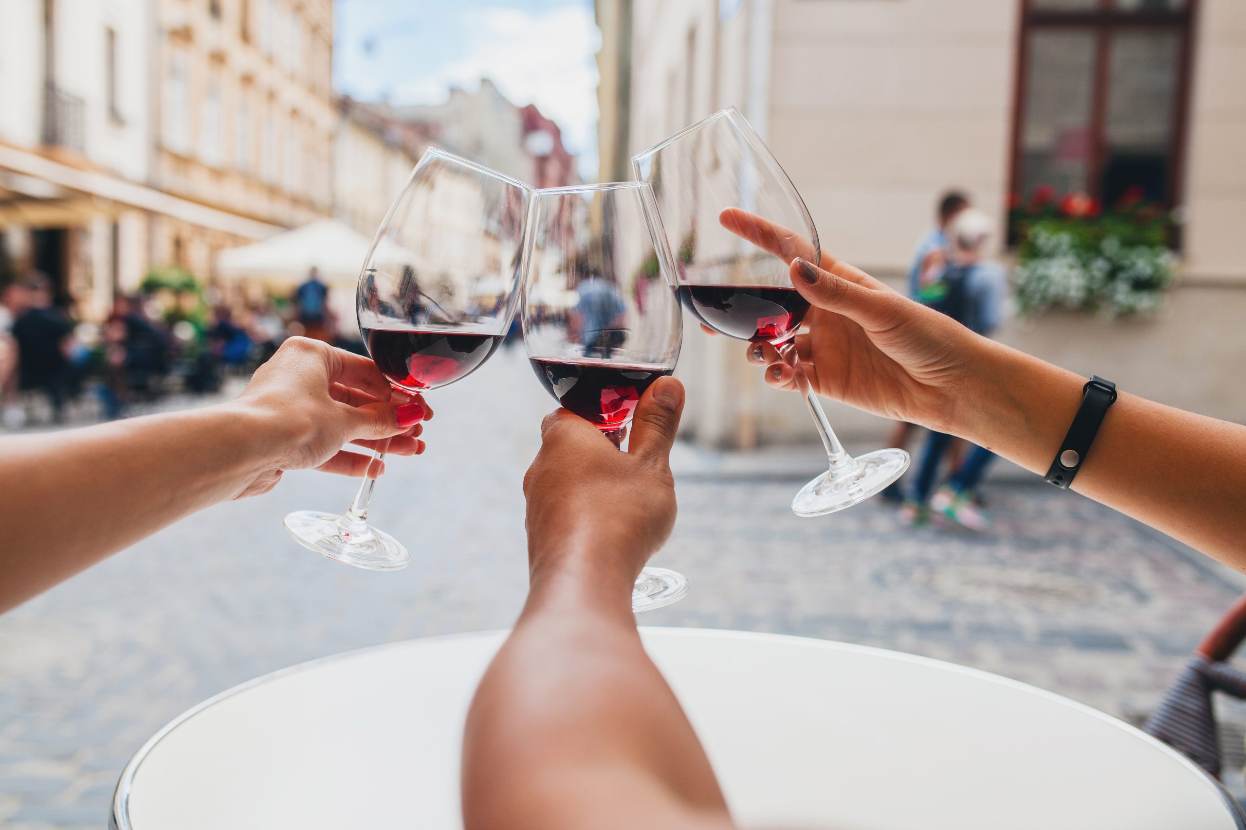 young hipster company of friends sitting in city street cafe, close up hands holding glasses, toasting, celebrating, drinking wine, summer vacation, party, having fun, details